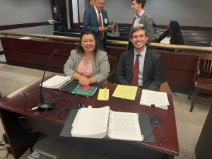 Attorneys Rachelle Miller and Wilson Landers seated at counsel table during the 2025 Primerus Trial Skills Academy mock trial at Mercer Law School, with trial materials and microphones in front of them and faculty and participants in the background.